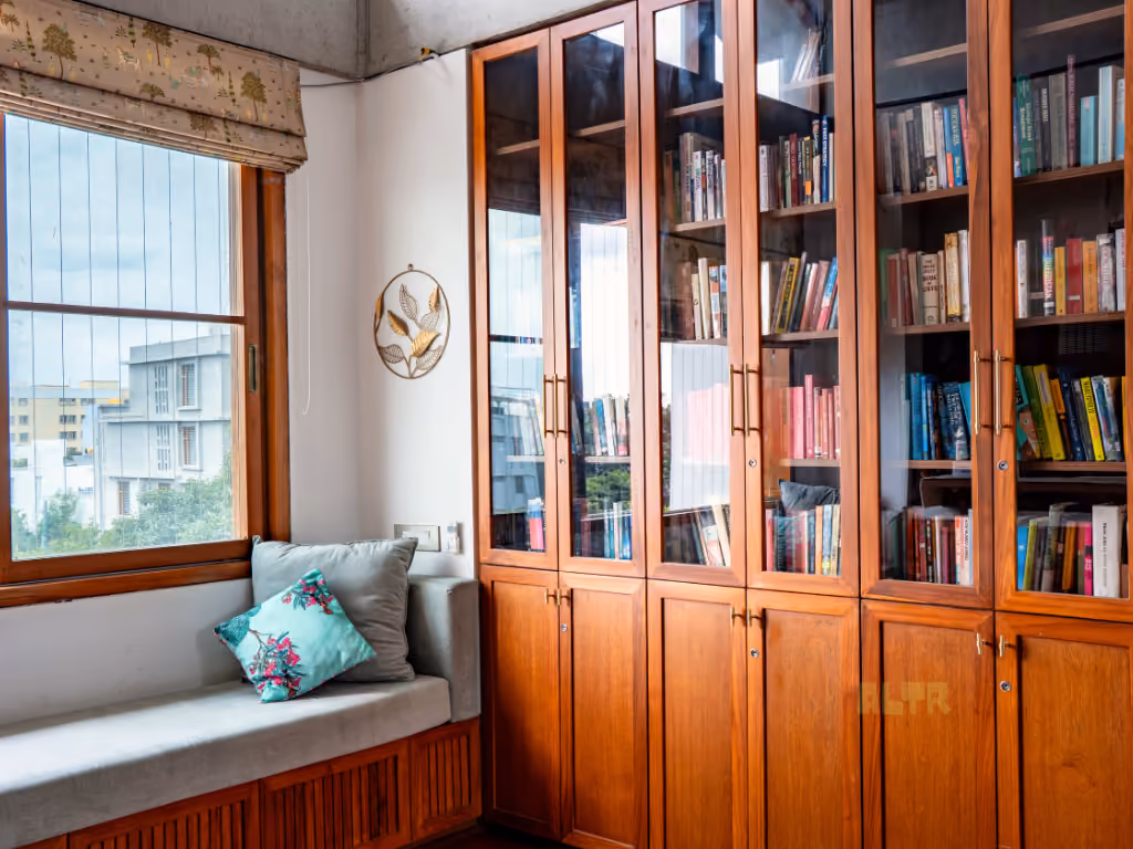 A window seat with cushions beside tall glass-fronted bookshelves